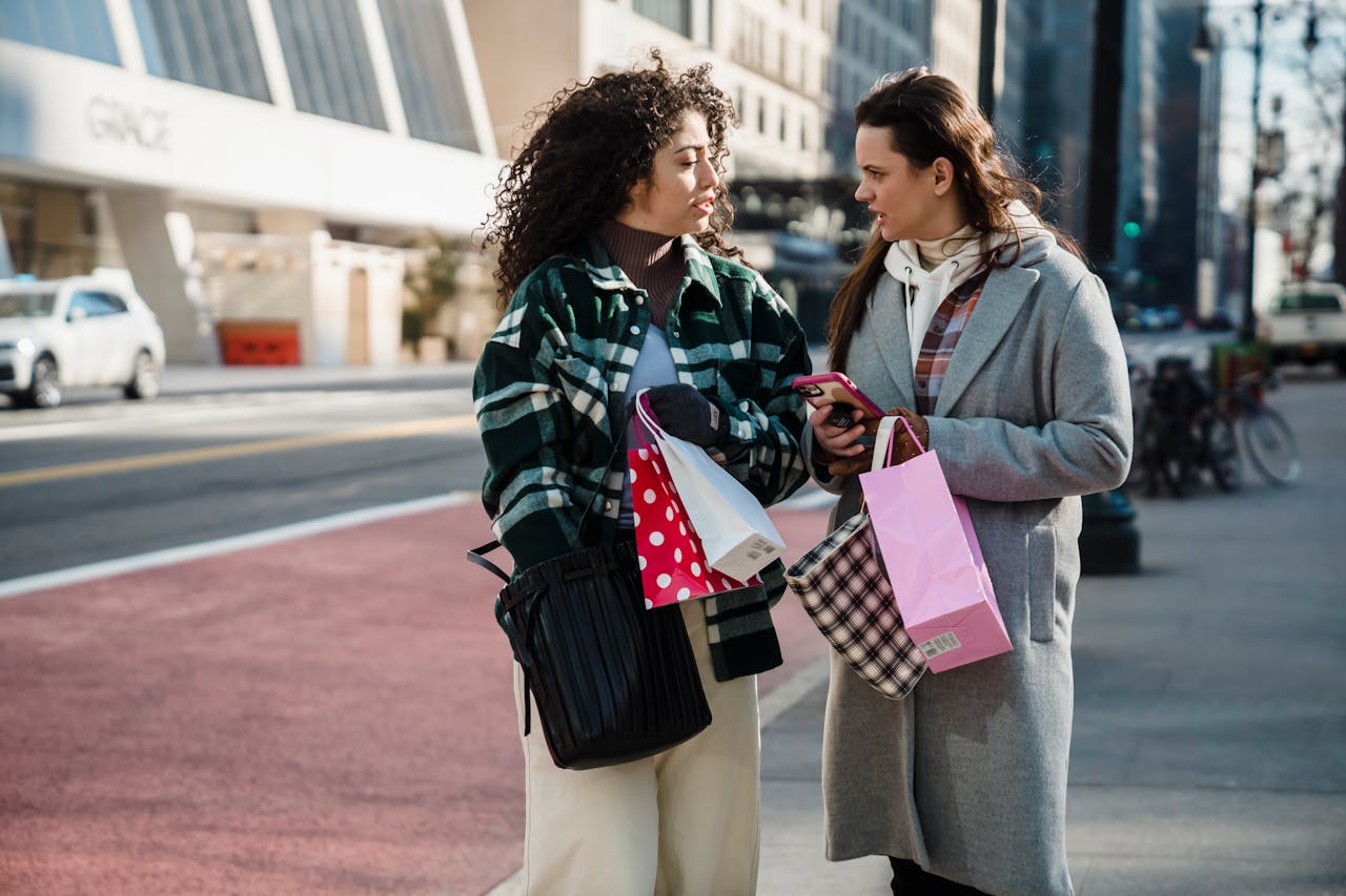 Two women chatting and carrying shopping bags in a lively urban street scene.